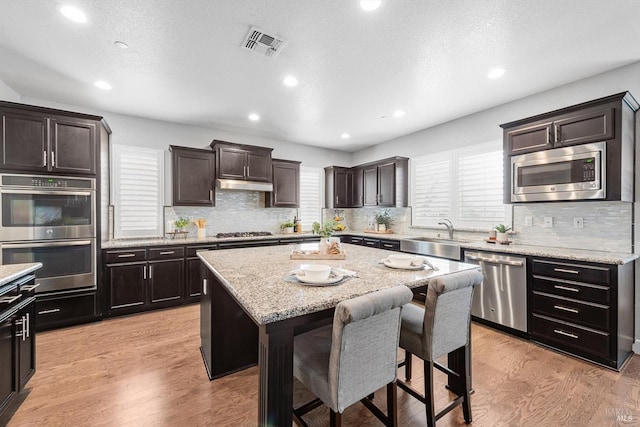 kitchen featuring light wood finished floors, stainless steel appliances, visible vents, a sink, and under cabinet range hood