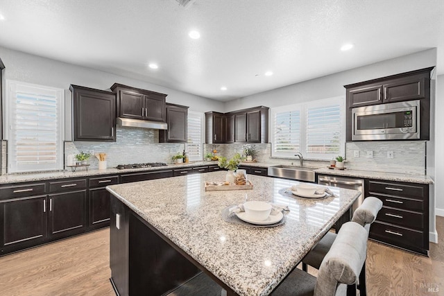 kitchen featuring under cabinet range hood, light wood-style flooring, appliances with stainless steel finishes, and a sink