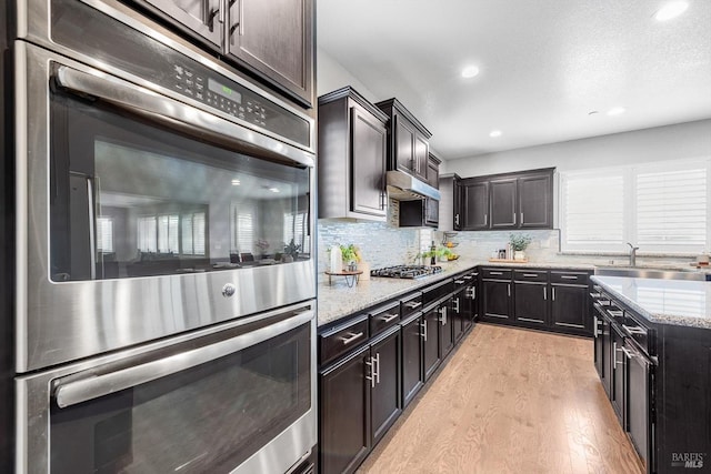 kitchen featuring tasteful backsplash, light stone countertops, stainless steel appliances, light wood-style floors, and a sink