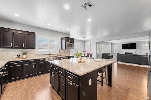 kitchen featuring a breakfast bar area, a sink, visible vents, light wood-style floors, and stainless steel microwave