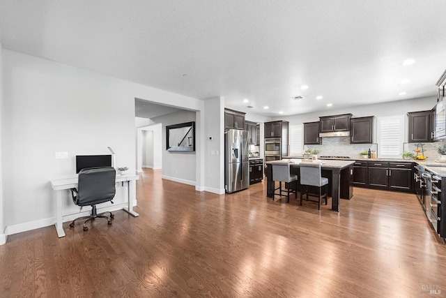 kitchen featuring a kitchen island, dark wood-type flooring, stainless steel appliances, dark brown cabinets, and a kitchen bar