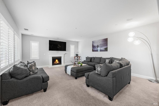 living area featuring a fireplace with flush hearth, a healthy amount of sunlight, light carpet, and visible vents