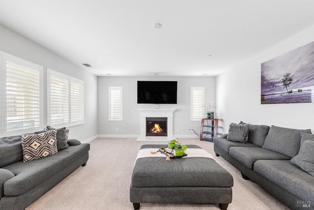 living room featuring baseboards, a glass covered fireplace, visible vents, and light colored carpet