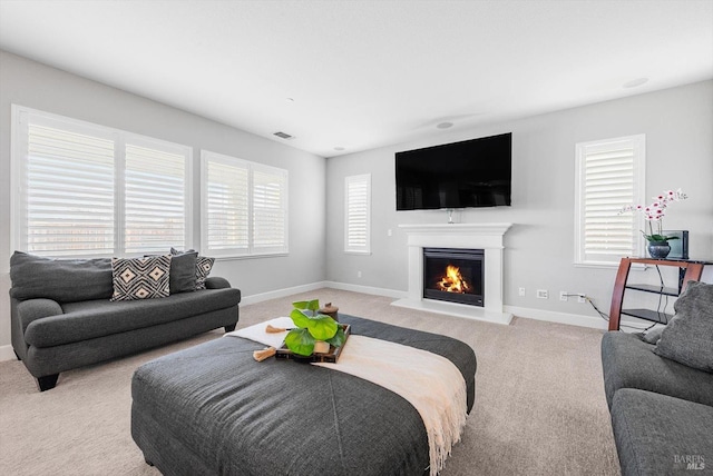 living area with light carpet, visible vents, baseboards, and a glass covered fireplace