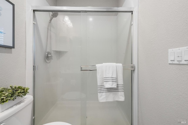 bathroom with toilet, a shower stall, and a textured wall