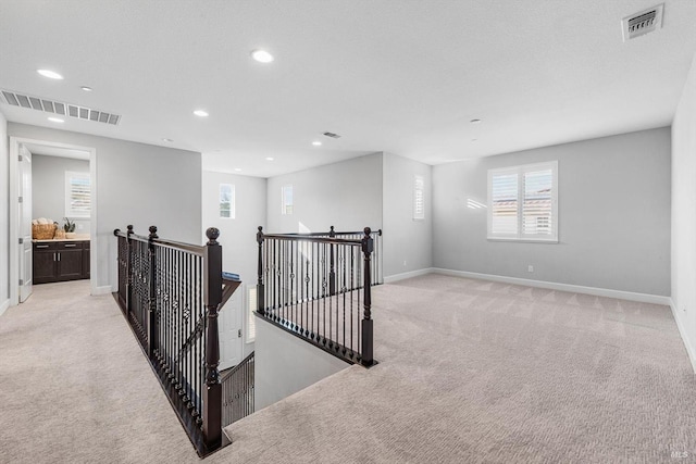 hallway with baseboards, visible vents, light colored carpet, and an upstairs landing