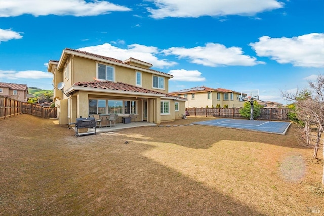 rear view of property with basketball hoop, a tiled roof, a fenced backyard, and stucco siding