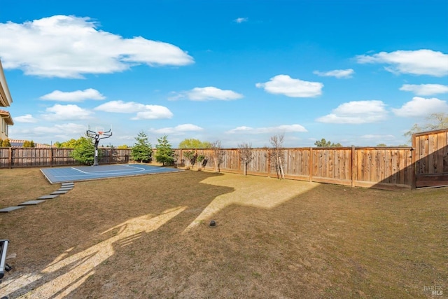 view of yard with a fenced backyard and basketball hoop