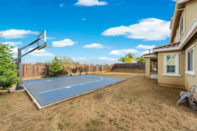 view of basketball court with basketball hoop, a fenced backyard, and a yard