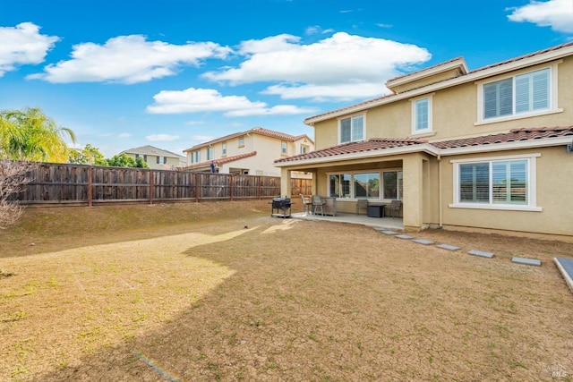 rear view of property with stucco siding, a lawn, a patio area, a fenced backyard, and a tiled roof