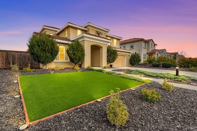 mediterranean / spanish house featuring fence, concrete driveway, a tiled roof, a lawn, and stucco siding