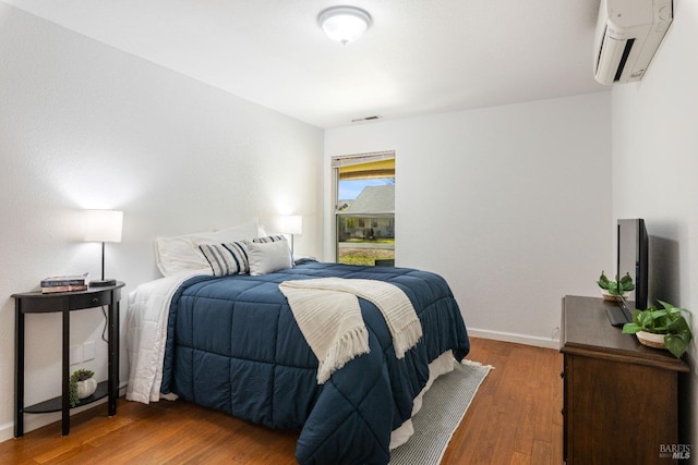 bedroom featuring baseboards, visible vents, an AC wall unit, and wood finished floors