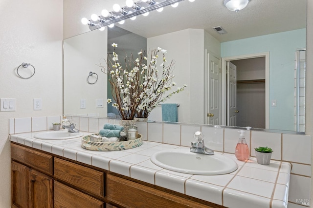 full bathroom featuring a textured ceiling, double vanity, a sink, and visible vents