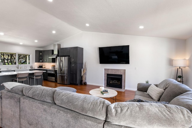 living area with dark wood-style floors, vaulted ceiling, a tiled fireplace, and recessed lighting