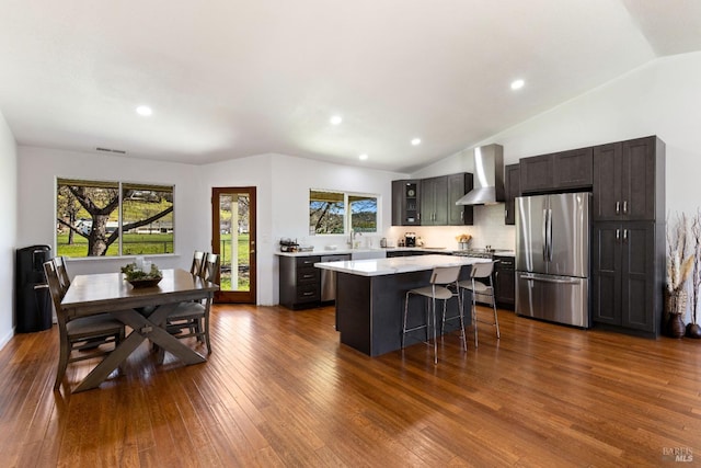 kitchen with a kitchen island, a breakfast bar, stainless steel appliances, light countertops, and wall chimney range hood