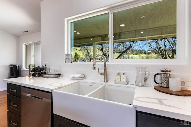 kitchen with visible vents, wood finished floors, light stone countertops, stainless steel dishwasher, and a sink