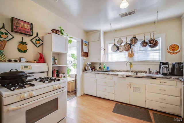 kitchen with white gas stove, visible vents, light wood-style floors, a sink, and plenty of natural light