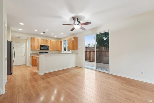 kitchen with light wood-style flooring, freestanding refrigerator, black microwave, a peninsula, and baseboards