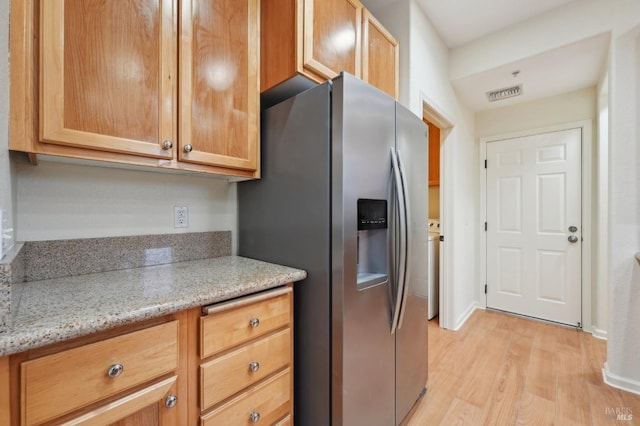 kitchen with light wood-style floors, visible vents, stainless steel refrigerator with ice dispenser, and light stone counters