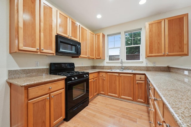 kitchen with light stone counters, recessed lighting, light wood-style floors, a sink, and black appliances