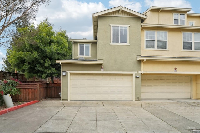 view of front facade featuring a garage, driveway, fence, and stucco siding