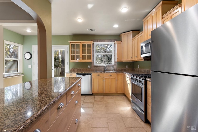 kitchen featuring arched walkways, light tile patterned floors, stainless steel appliances, visible vents, and a sink