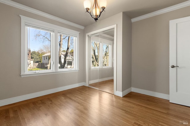 unfurnished dining area featuring a notable chandelier, baseboards, wood finished floors, and ornamental molding