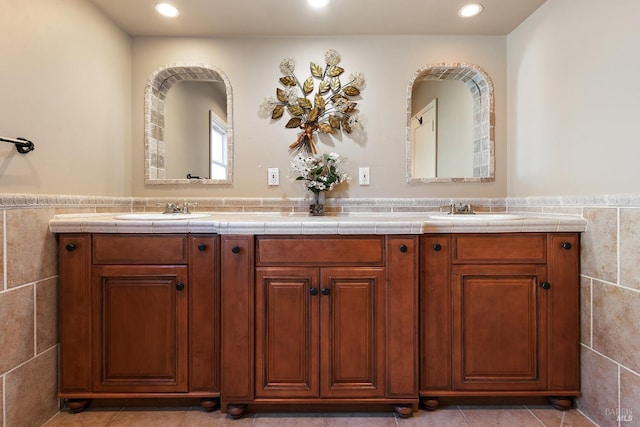 full bath featuring double vanity, a sink, and tile walls