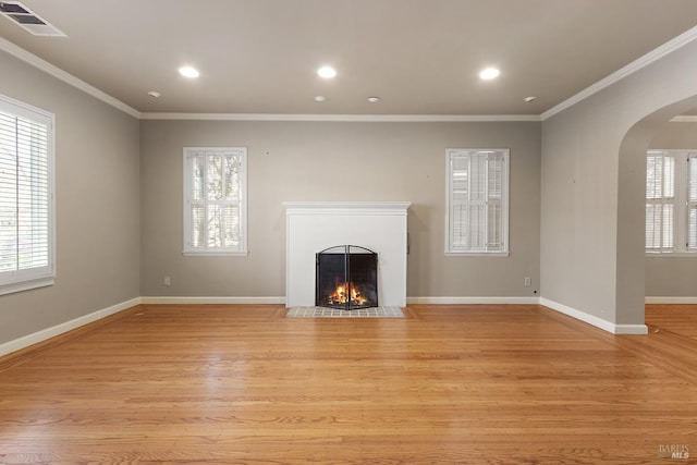 unfurnished living room with arched walkways, visible vents, a fireplace with flush hearth, ornamental molding, and light wood-type flooring