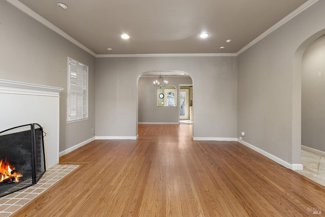 unfurnished living room with arched walkways, crown molding, a tiled fireplace, and baseboards