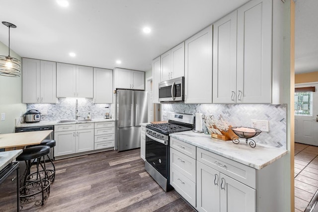 kitchen with stainless steel appliances, dark wood-type flooring, a sink, decorative backsplash, and decorative light fixtures