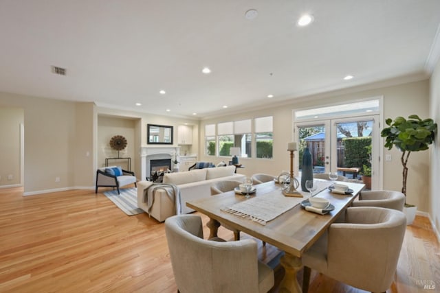 dining room with a glass covered fireplace, french doors, light wood-style flooring, and baseboards