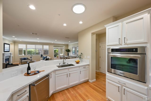 kitchen with a warm lit fireplace, appliances with stainless steel finishes, open floor plan, light countertops, and a sink