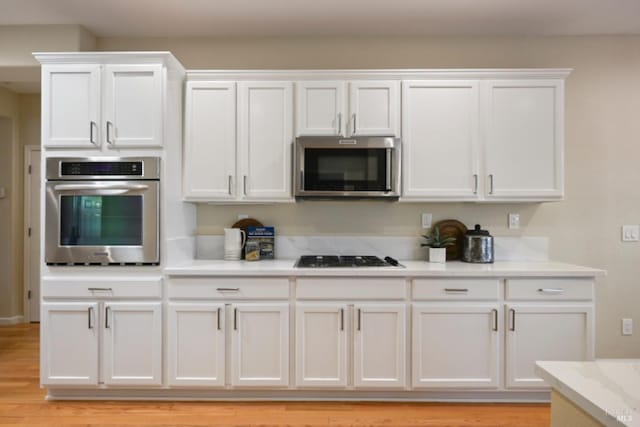 kitchen with stainless steel appliances, light wood-type flooring, white cabinets, and light stone counters