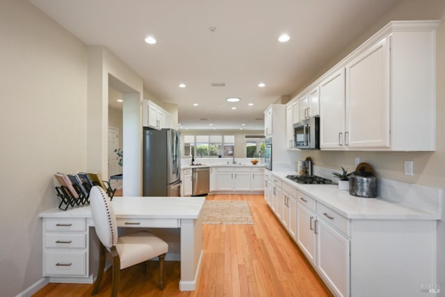 kitchen with a peninsula, appliances with stainless steel finishes, light wood-style floors, and white cabinets