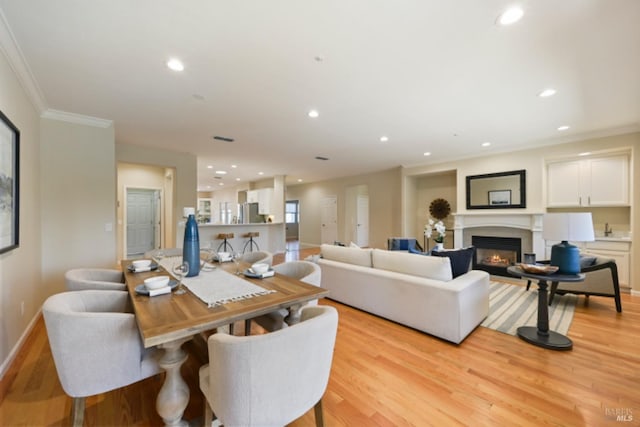 living area featuring light wood-style floors, recessed lighting, a glass covered fireplace, and ornamental molding