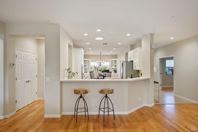 kitchen featuring light wood-type flooring, freestanding refrigerator, white cabinetry, and a breakfast bar