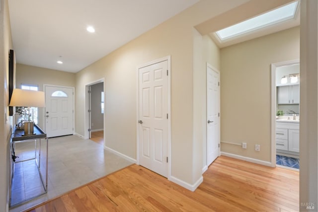 foyer entrance with light wood-style floors, a skylight, baseboards, and recessed lighting