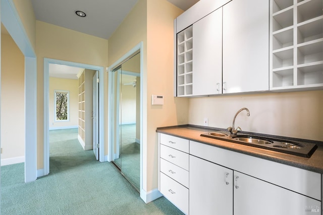 kitchen featuring light colored carpet, a sink, white cabinetry, baseboards, and open shelves