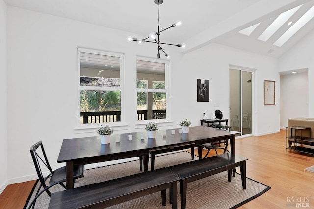 dining room with vaulted ceiling with skylight, light wood-style floors, baseboards, and a chandelier