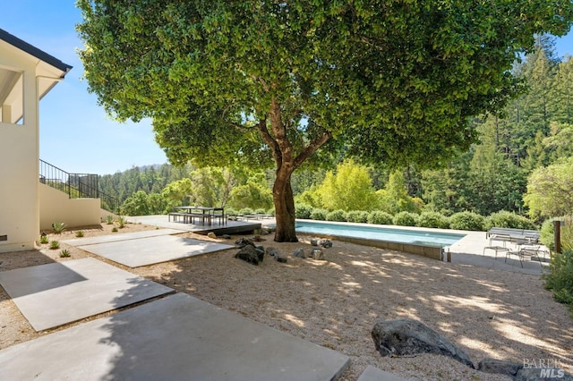 view of yard featuring a patio, an outdoor pool, and a wooded view