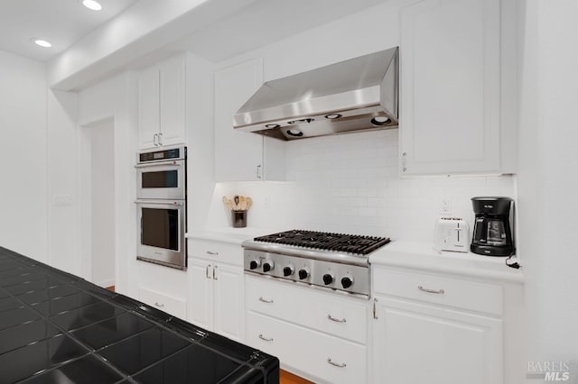 kitchen with wall chimney range hood, stainless steel appliances, white cabinets, light countertops, and decorative backsplash