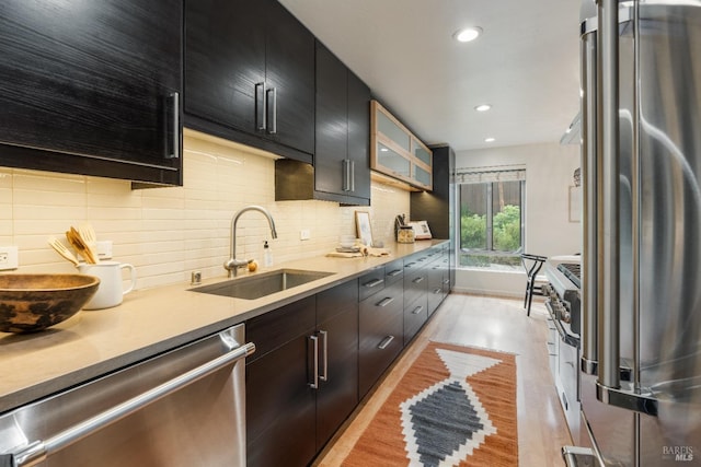 kitchen with backsplash, appliances with stainless steel finishes, a sink, light wood-type flooring, and dark cabinetry