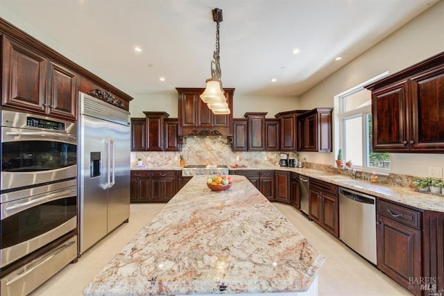 kitchen featuring pendant lighting, light stone counters, backsplash, a center island, and stainless steel appliances