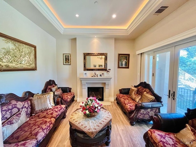 living room with visible vents, light wood-style flooring, ornamental molding, a tray ceiling, and french doors