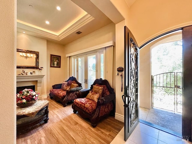 interior space featuring visible vents, french doors, light wood-style floors, a fireplace, and a raised ceiling