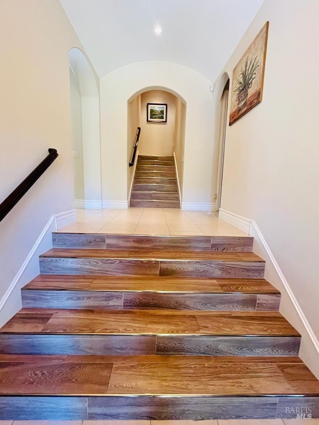 stairs with arched walkways, tile patterned floors, baseboards, and vaulted ceiling