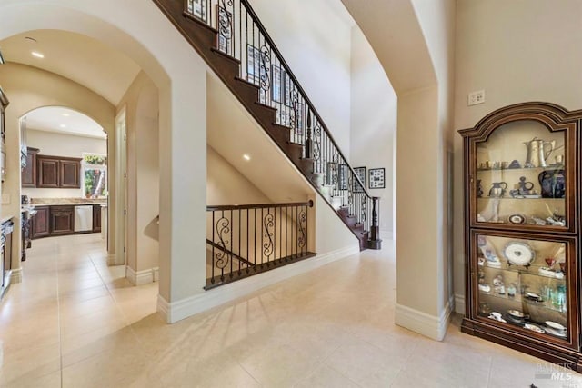hallway featuring baseboards, arched walkways, light tile patterned flooring, and a towering ceiling