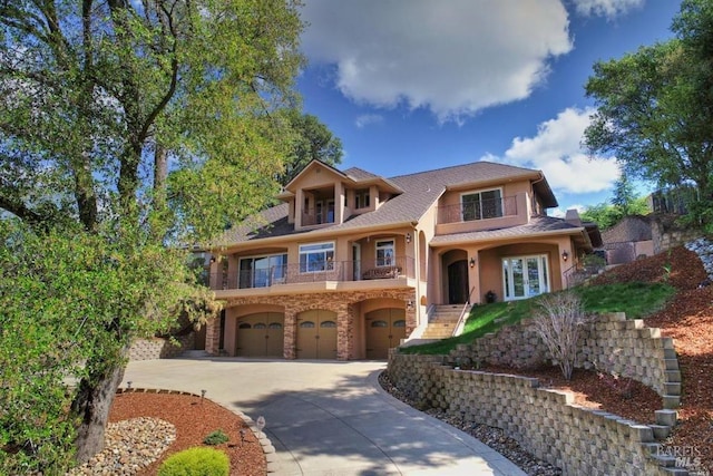 view of front of home with an attached garage, a balcony, concrete driveway, stone siding, and stucco siding