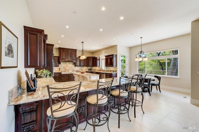 kitchen featuring backsplash, light stone countertops, a kitchen bar, a peninsula, and hanging light fixtures